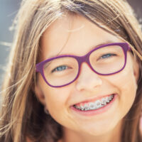 Happy smiling girl with dental braces and glasses. Young cute caucasian blond girl wearing teeth braces and glasses.